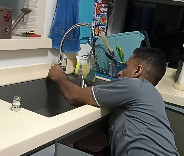 Plumber leaning over a kitchen counter to repair and secure a sink tap faucet in Singapore.
