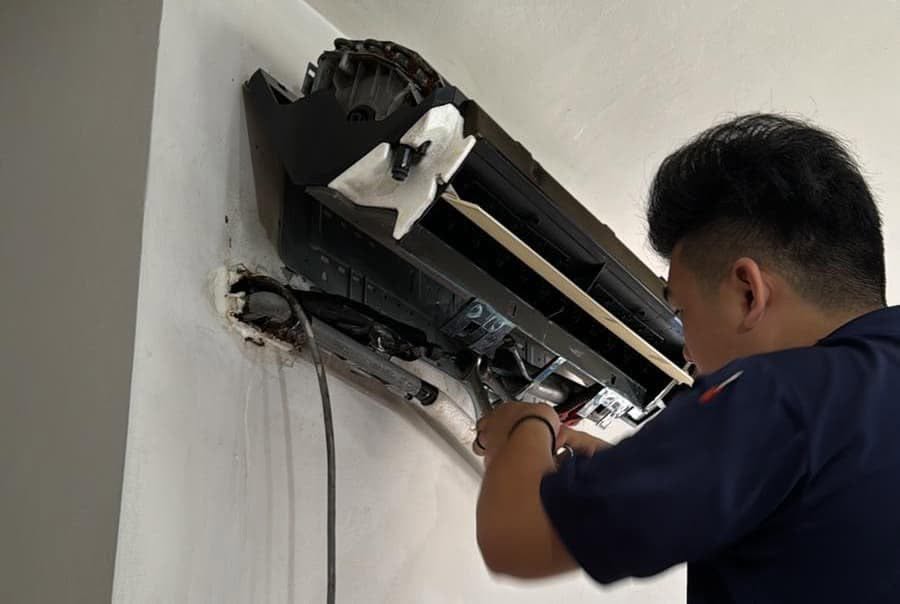 Aircon technician servicing and repairing an open wall-mounted air conditioner unit in Singapore.
