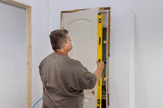 Carpentering technician using a yellow spirit level to check alignment during interior wooden door frame installation.