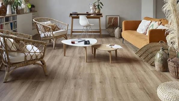 Boho-chic living room interior with light wood laminate vinyl flooring, rattan armchairs, wooden coffee tables, and a mustard yellow sofa.