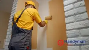 Professional painter in yellow shirt and overalls applying warm brown paint to an interior wall using a roller in Singapore.